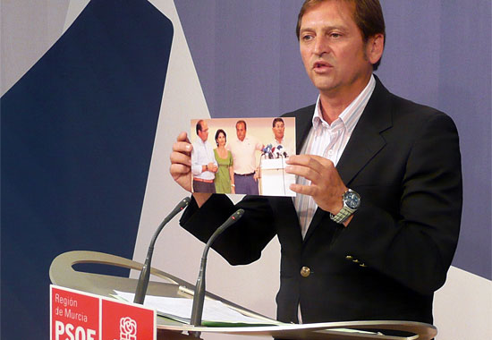 Ramón Román, portavoz municipal de Águilas, muestra la fotografía del anuncio del Pacto de gobierno en Águilas, en la que aparecen la consejera Inmaculada García, el alcalde Juan Ramírez, Pedro Antonio Sánchez, y el tránsfuga Clemente García.